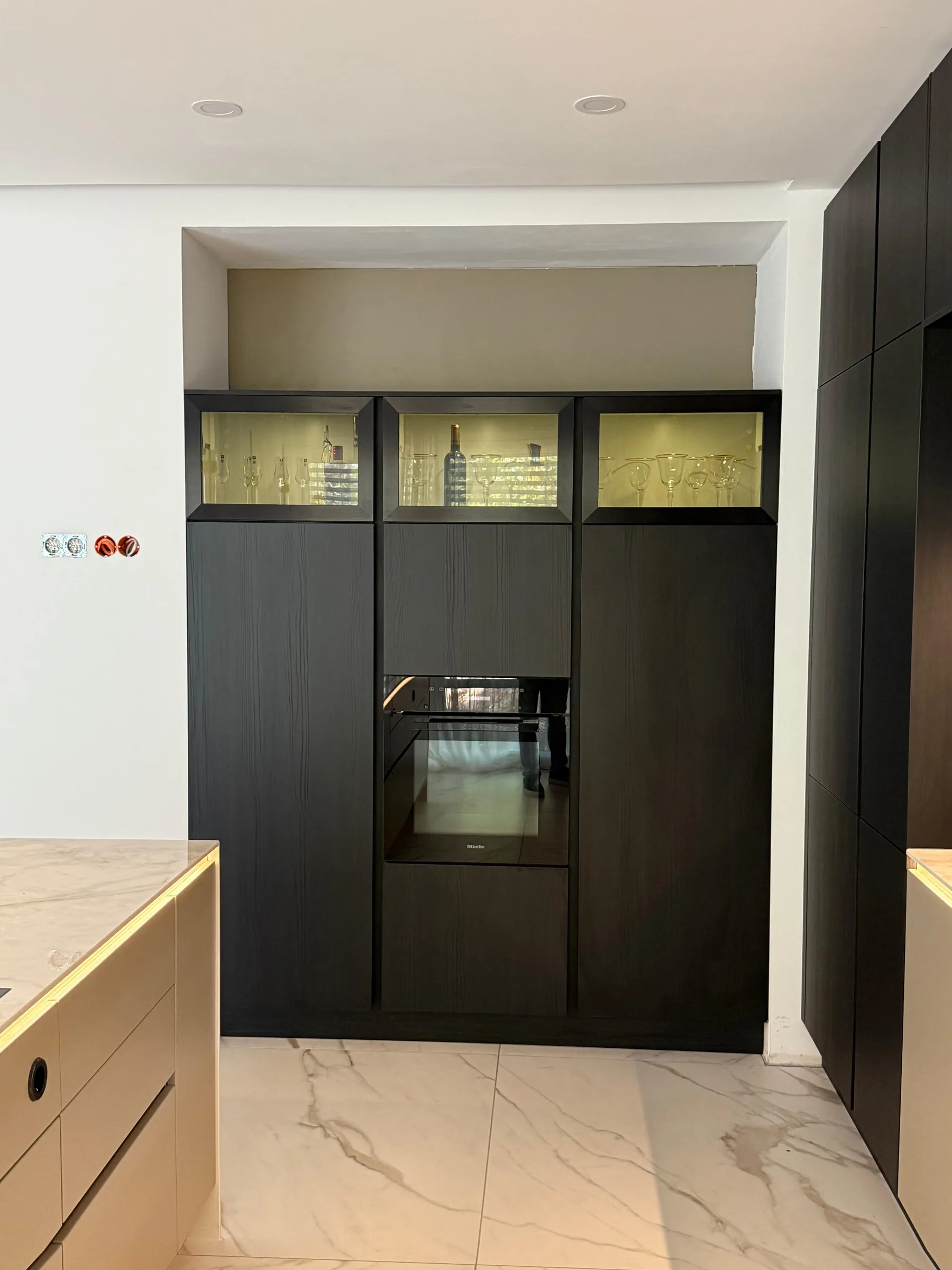 Hochschrankwand in schwarzem Holz mit beleuchteten Vitrinen und Miele Backofen