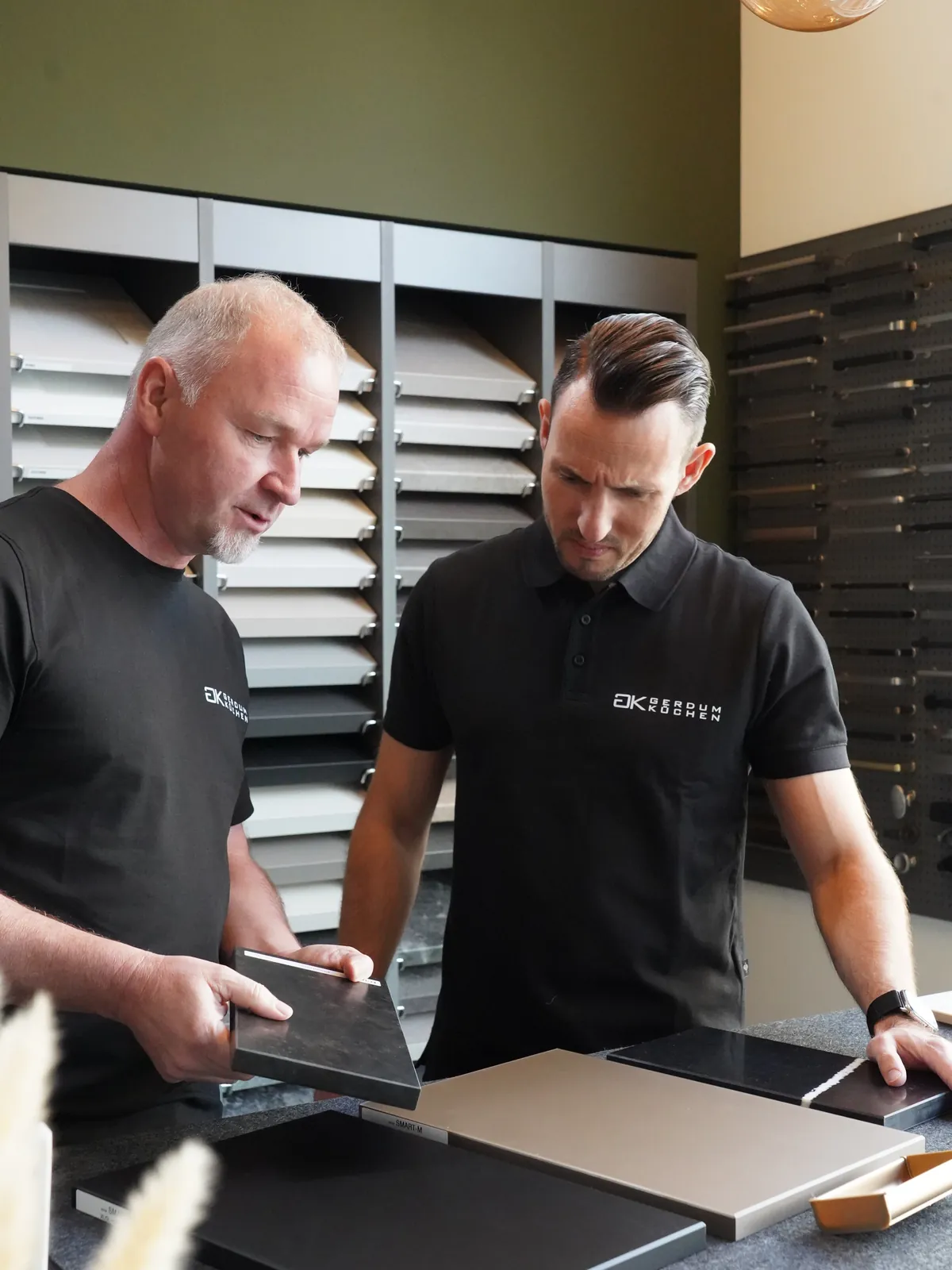 Zwei Mitarbeiter von Gerdum Küchen bei der Materialauswahl an der Musterwand